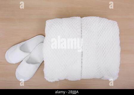 Folded bathrobe and bathing slippers on wooden background Stock Photo