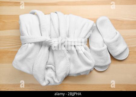 Folded white bathrobe and spa slippers on wooden background Stock Photo