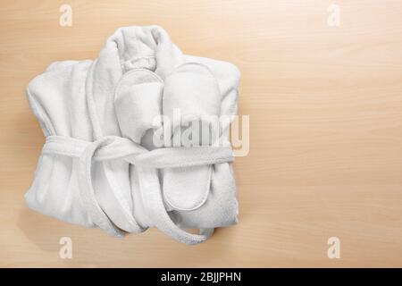 Folded white bathrobe and spa slippers on wooden background Stock Photo