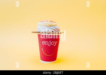 white pastry souffle with cream and fresh strawberries and a red paper Cup with the words Enjoy on a soft yellow background. Stock Photo