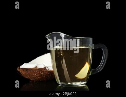 Ripe coconut and pitcher with oil on black background Stock Photo