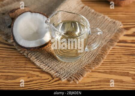 Ripe coconut and pitcher with oil on wooden background Stock Photo