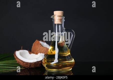 Ripe coconut and pitcher with oil on black background Stock Photo