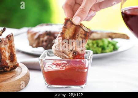 Woman dipping ribs into ketchup on table Stock Photo