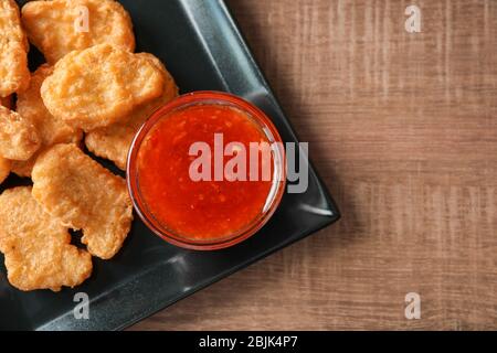 Plate with chicken nuggets and chili sauce on kitchen table Stock Photo