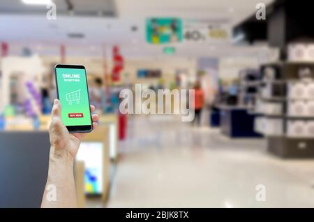 Holding a touch screen smartphone with online shopping word on a shopping mall background. Stock Photo