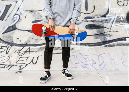 Close up of unrecognizable young man holding skateboard in the park.