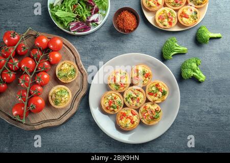Composition with broccoli quiche tartlets and vegetables on table Stock Photo