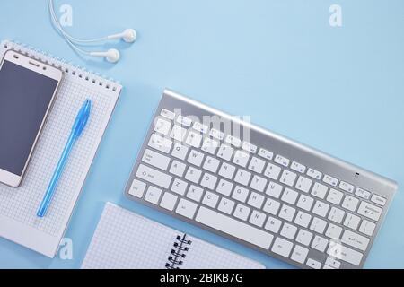 Minimal work space. Creative flat lay photo of workspace desk. Top view office desk with notepad, keyboard, paper notepad and supplies on blue color b Stock Photo