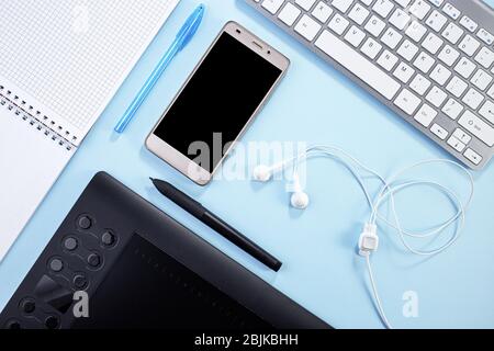 Minimal work space. Creative flat lay photo of workspace desk. Top view office desk with notepad, keyboard, graphic tablet and paper notepad on blue c Stock Photo