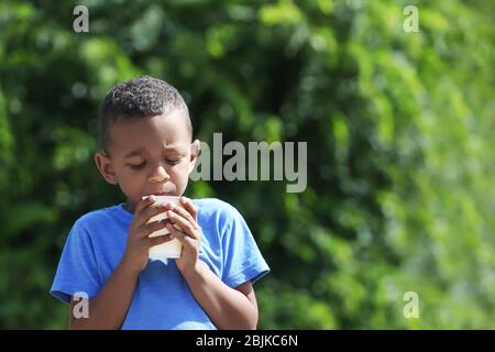 Cute African American boy drinking water from plastic cup, outdoors Stock Photo