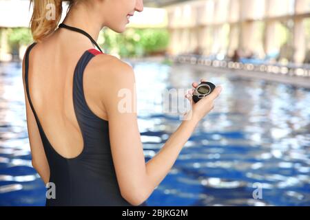 Beautiful young coach with stopwatch standing near swimming pool Stock Photo