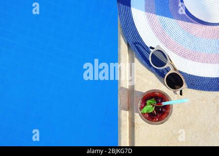 Sunglasses, straw hat and glass of cocktail near swimming pool Stock Photo