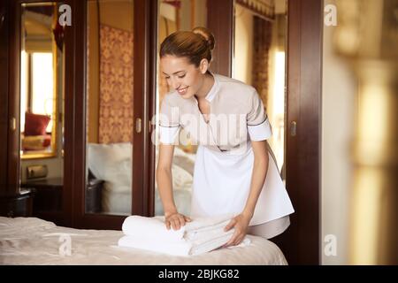 Chambermaid putting clean towels on bed in hotel room Stock Photo