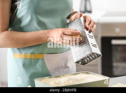 Woman grating cheese for lasagna in kitchen Stock Photo