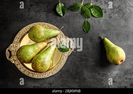 Composition with ripe pears and ornate metal plate on dark background Stock Photo