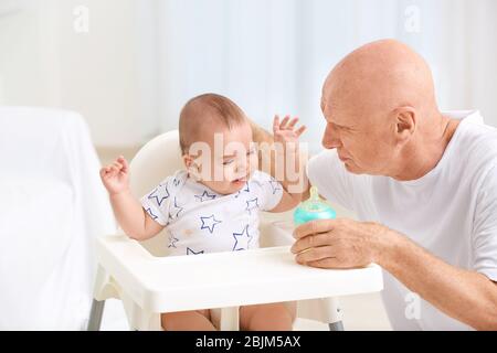 Senior man giving drink to his little grandchild at home Stock Photo