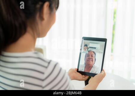 Asian young woman virtual happy hour meeting and talking online together with her mother in video conference with digital tablet for a online meeting Stock Photo