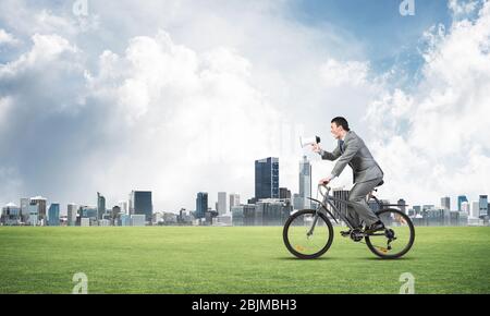 Businessman with megaphone on bike Stock Photo