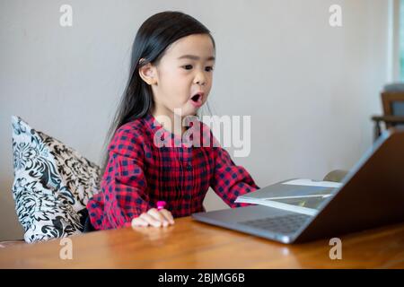 Asian girl or daughters use notebooks and technology for online learning during school holidays and watching cartoons at home. Educational concepts an Stock Photo