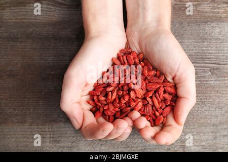 Hands of woman holding red dried goji berries on wooden background. Heart health concept Stock Photo