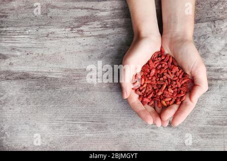 Hands of woman holding red dried goji berries on wooden background Stock Photo