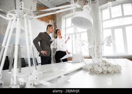 Spacious housing. Female estate agent showing new home to a young man after a discussion on house plans. Choosing construction materials, repair, technologies in smart house. Moving, new home concept. Stock Photo