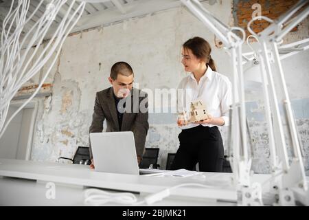 Spacious housing. Female estate agent showing new home to a young man after a discussion on house plans. Choosing construction materials, repair, technologies in smart house. Moving, new home concept. Stock Photo