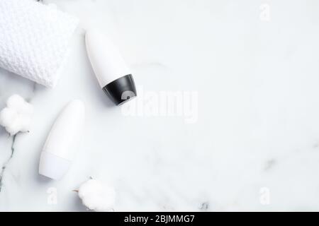 Roll-on deodorant bottles with cotton flowers and towel on marble background. Flat lay, top view. Underarm skin care, sweat protection concept Stock Photo