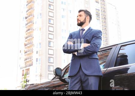 Handsome young man in elegant suit standing near car outdoors Stock Photo