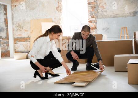 Repairs details. Female estate agent showing new home to a young man after a discussion on house plans. Choosing construction materials, repair, technologies in smart house. Moving, new home concept. Stock Photo