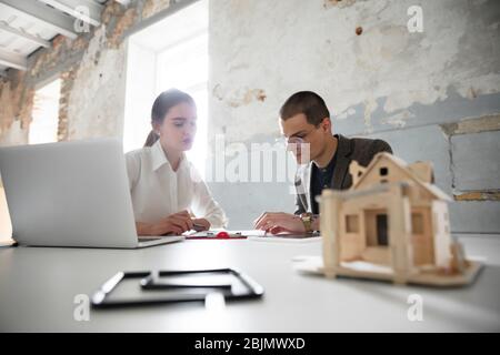 New solutions. Female estate agent showing new home to a young man after a discussion on house plans. Choosing construction materials, repair, technologies in smart house. Moving, new home concept. Stock Photo