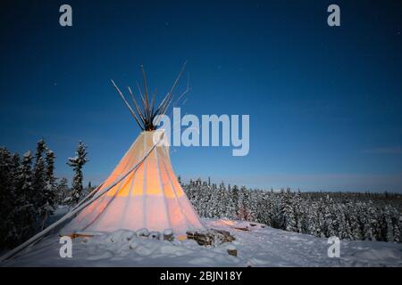 Glowing teepee in winter forest at night, Yellowknife, Northwest Territories, Canada