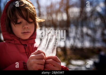 Boy standing in the forest holding a piece of frozen ice, USA Stock Photo