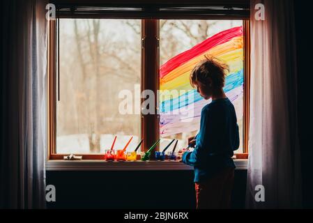 Boy painting a rainbow on a window, USA Stock Photo