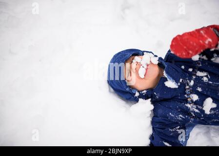 Happy boy lying on the ground covered in snow, USA