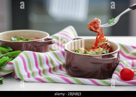 Fork with piece of delicious sausage casserole over cocotte on table Stock Photo