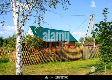 Beautiful summer country wooden house with an emerald roof, fence, birch, maple Stock Photo