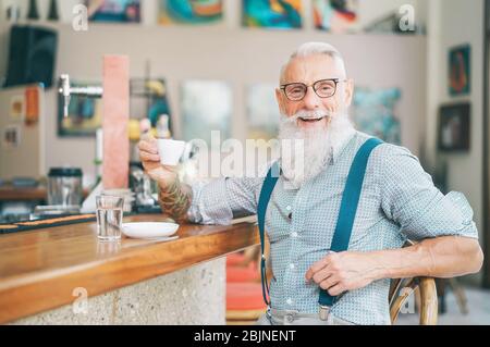 Senior bearded man drinking coffee sitting bar counter - Happy mature male having fun enjoying time outdoor Stock Photo