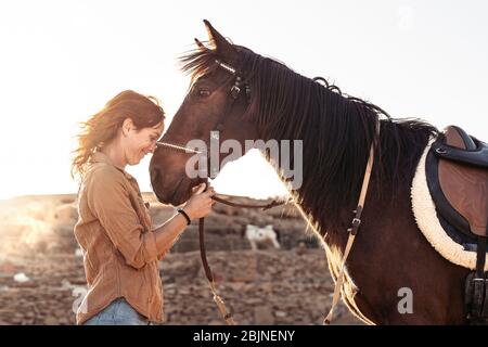 Young farmer cuddling her horse inside stable - Happy girl playing with animals in corral ranch - Human and animals relationship concept Stock Photo
