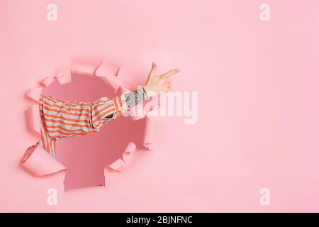 Male hand pointing, showing in torn coral paper hole background. Breaking on, breakthrought. Concept of celebration, shopping, proposal, sales, ad. Copyspace. Promotions discounts Stock Photo