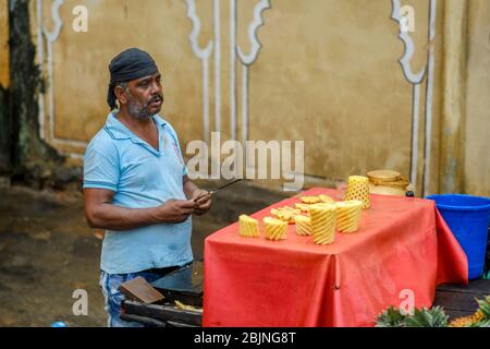 Jaipur, Rajasthan / India - September 29, 2019: Indian man sells freshly carved pineapples on street food fruit stall in Jaipur, India Stock Photo