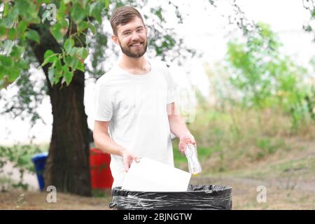 Young man throwing garbage into litter bin outdoors Stock Photo