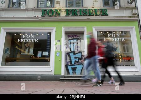 Hamburg, Germany. 28th Apr, 2020. Passers-by walk past a closed hairdresser in Ottensen (Hamburg-Altona) (shot with long exposure). The hairdressers of the Hanseatic city are closed because of the corona crisis. Credit: Bodo Marks/dpa/Alamy Live News Stock Photo