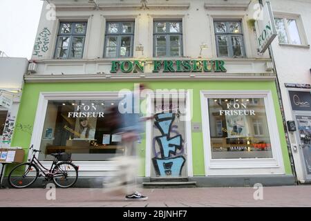 Hamburg, Germany. 28th Apr, 2020. A passer-by walks along a closed hairdresser's in Ottensen (Hamburg-Altona) (shot with long exposure). The hairdressers of the Hanseatic city are closed because of the corona crisis. Credit: Bodo Marks/dpa/Alamy Live News Stock Photo