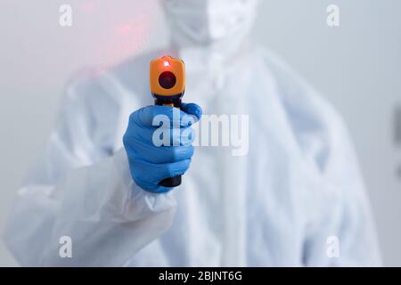 Mid section of a healthcare worker wearing a protective uniform, face mask and gloves against coronavirus, covid 19, holding a non contact thermometer Stock Photo