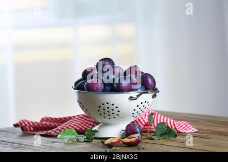 Fresh plums in colander on table Stock Photo
