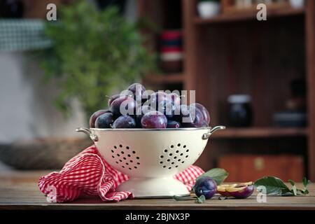 Fresh plums in colander on table Stock Photo