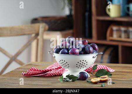 Fresh plums in colander on table Stock Photo