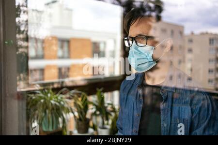 Man with face mask looking out of window Stock Photo